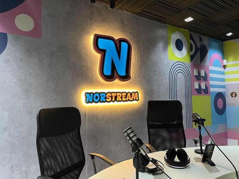 Set principal de Norstream con el isotipo y el logotipo iluminados, sillas, micrófonos y auriculares sobre la mesa